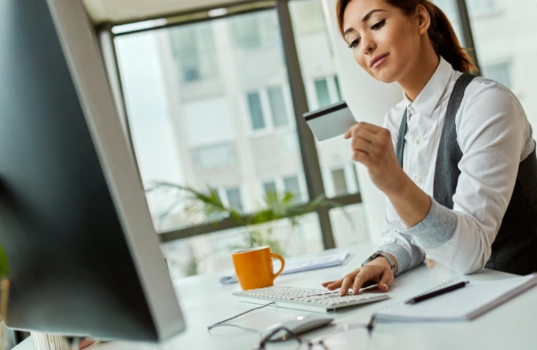 Smiling businesswoman using credit card and computer while buying on the internet in the office