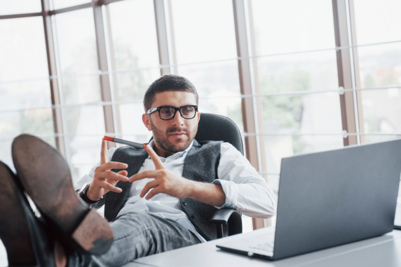 young businessman with glasses holding his legs on the table looking at a laptop in the office