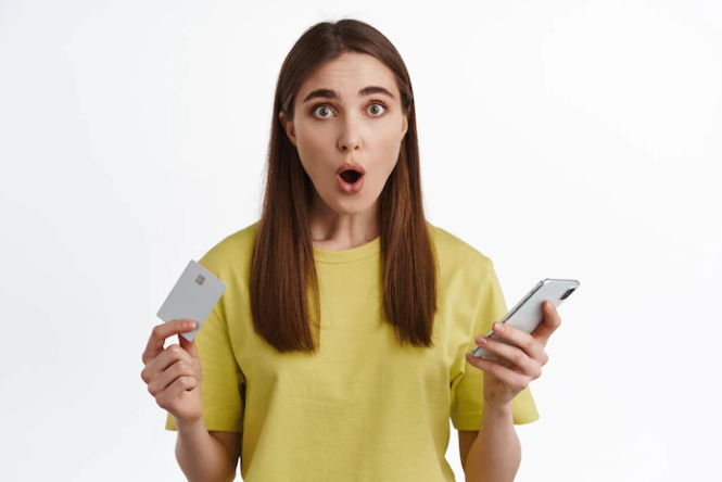 Amazed woman holding a smartphone and credit card standing against a white background